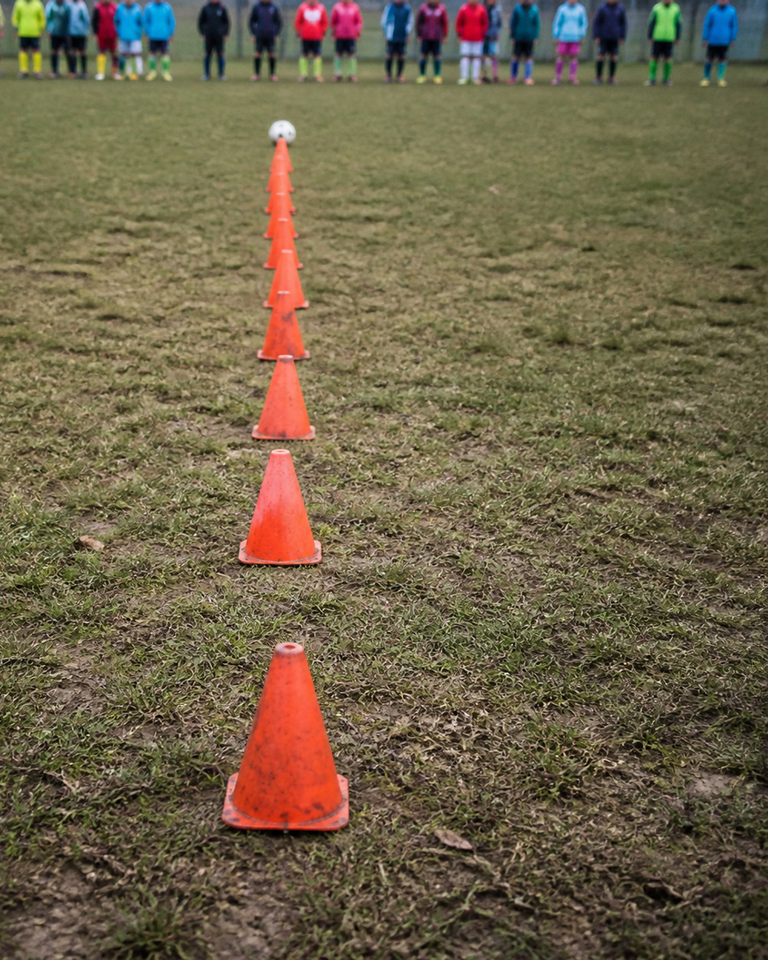 A long line of orange cones with one soccer ball at the far end